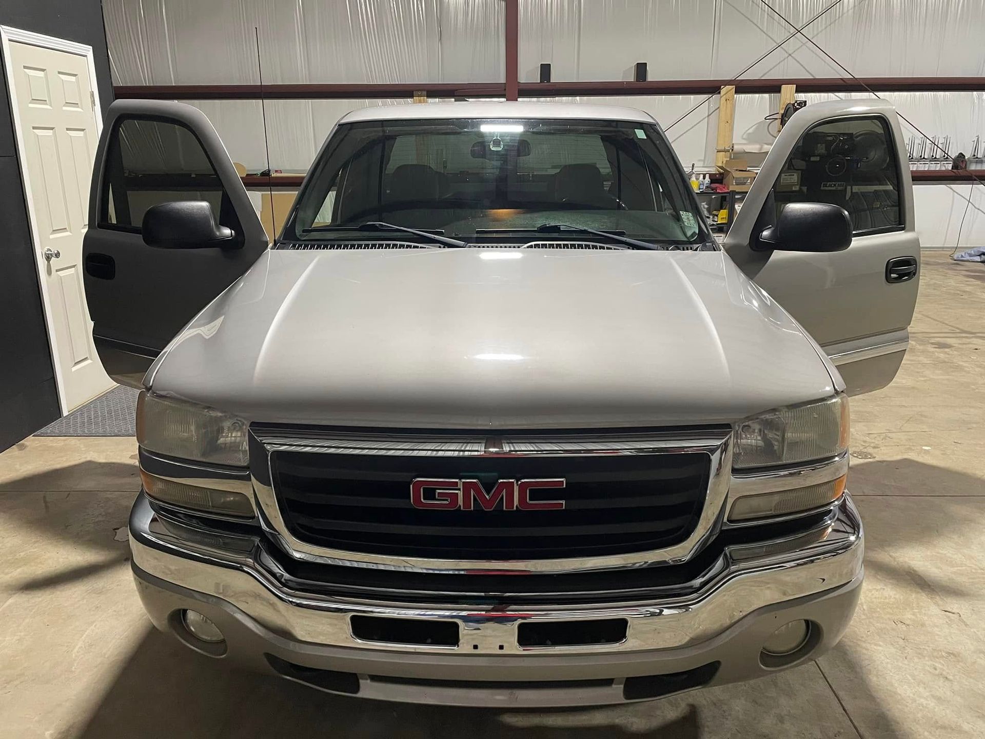 A silver gmc truck is parked in a garage with its doors open.