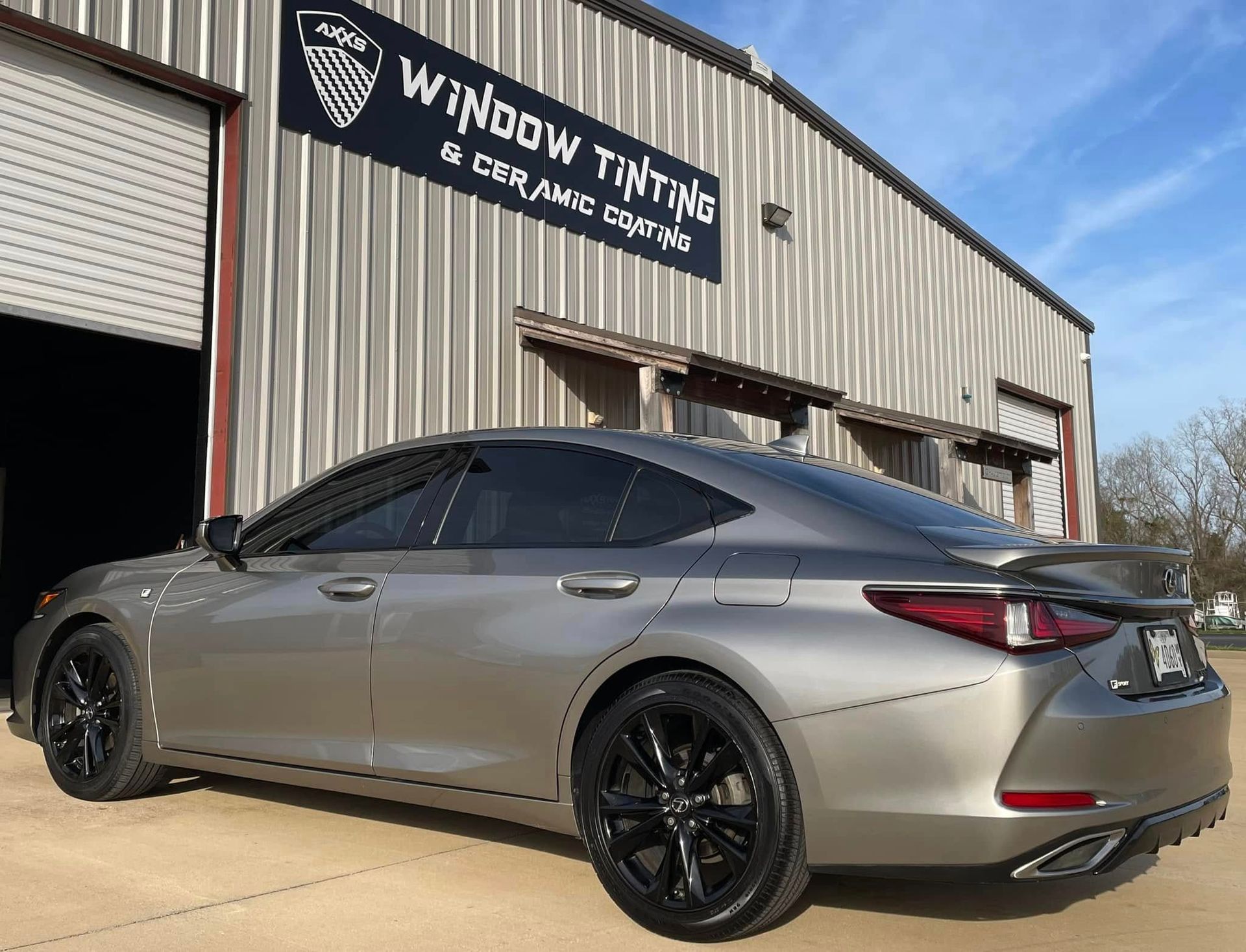 A silver car is parked in front of a building that says window tinting.