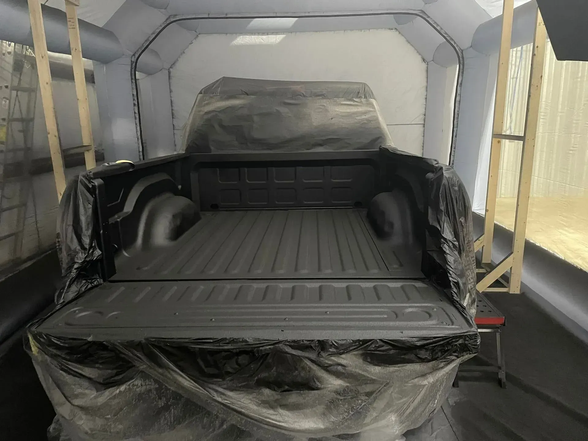 Truck bed covered in plastic, inside a spray booth, ready for painting.