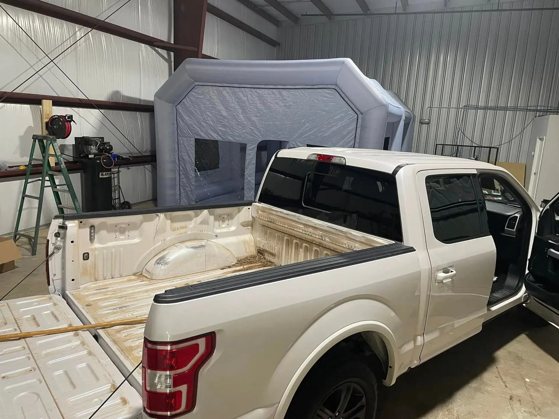 White pickup truck in a garage with an inflatable paint booth behind it.
