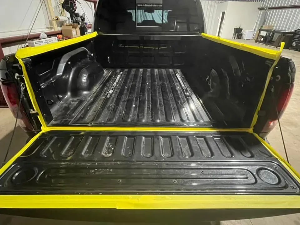 Black truck bed with yellow tape around the edges, prepared for painting.