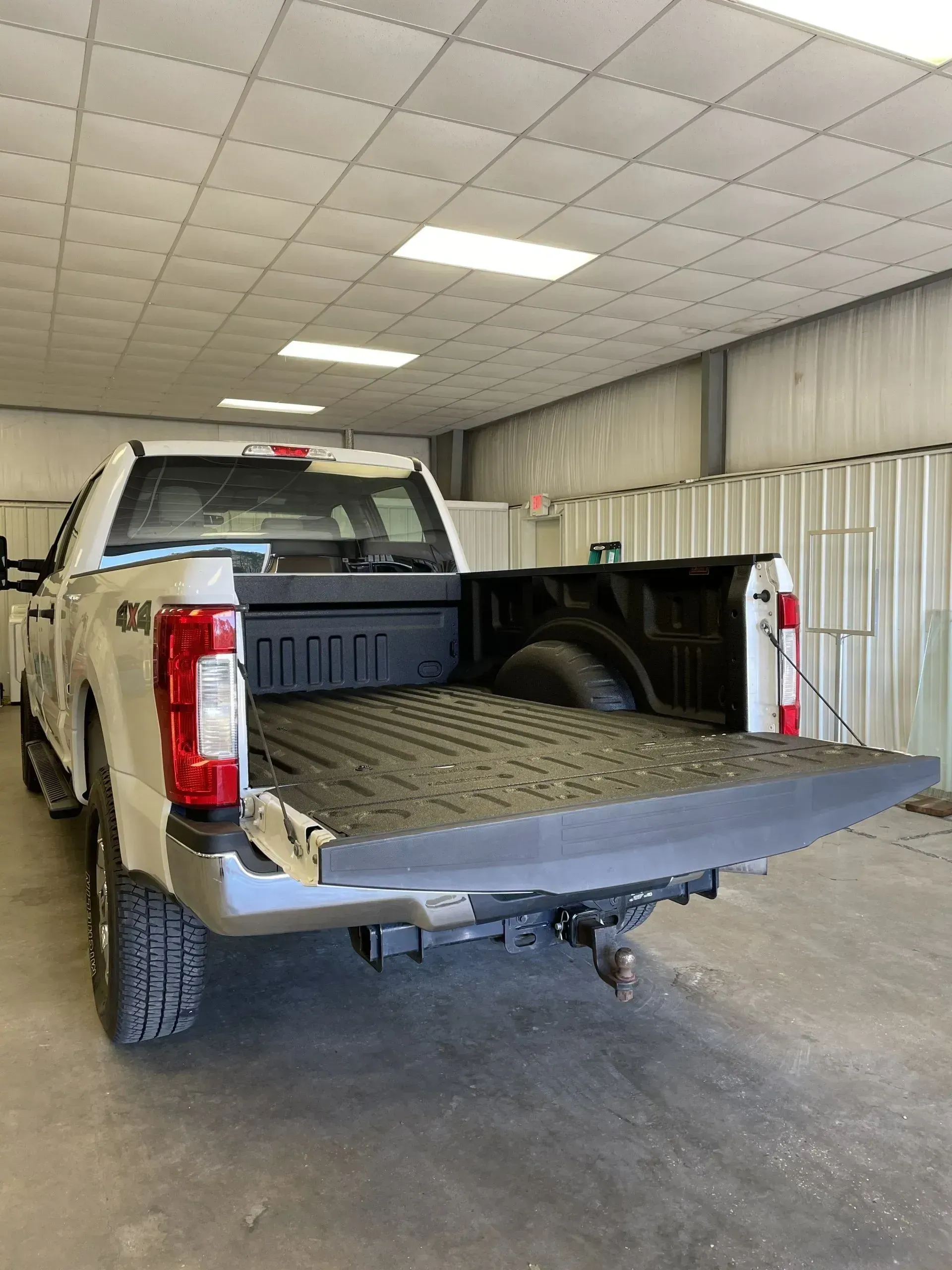A white truck is parked in a garage with its bed open.
