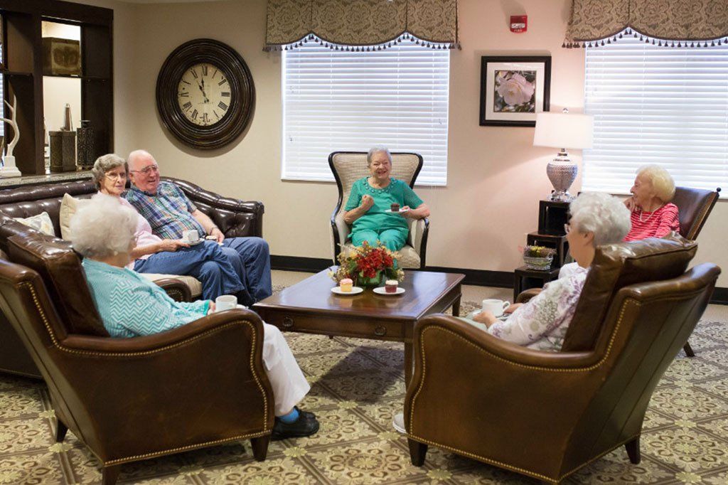 A group of elderly people are sitting around a coffee table in a living room.