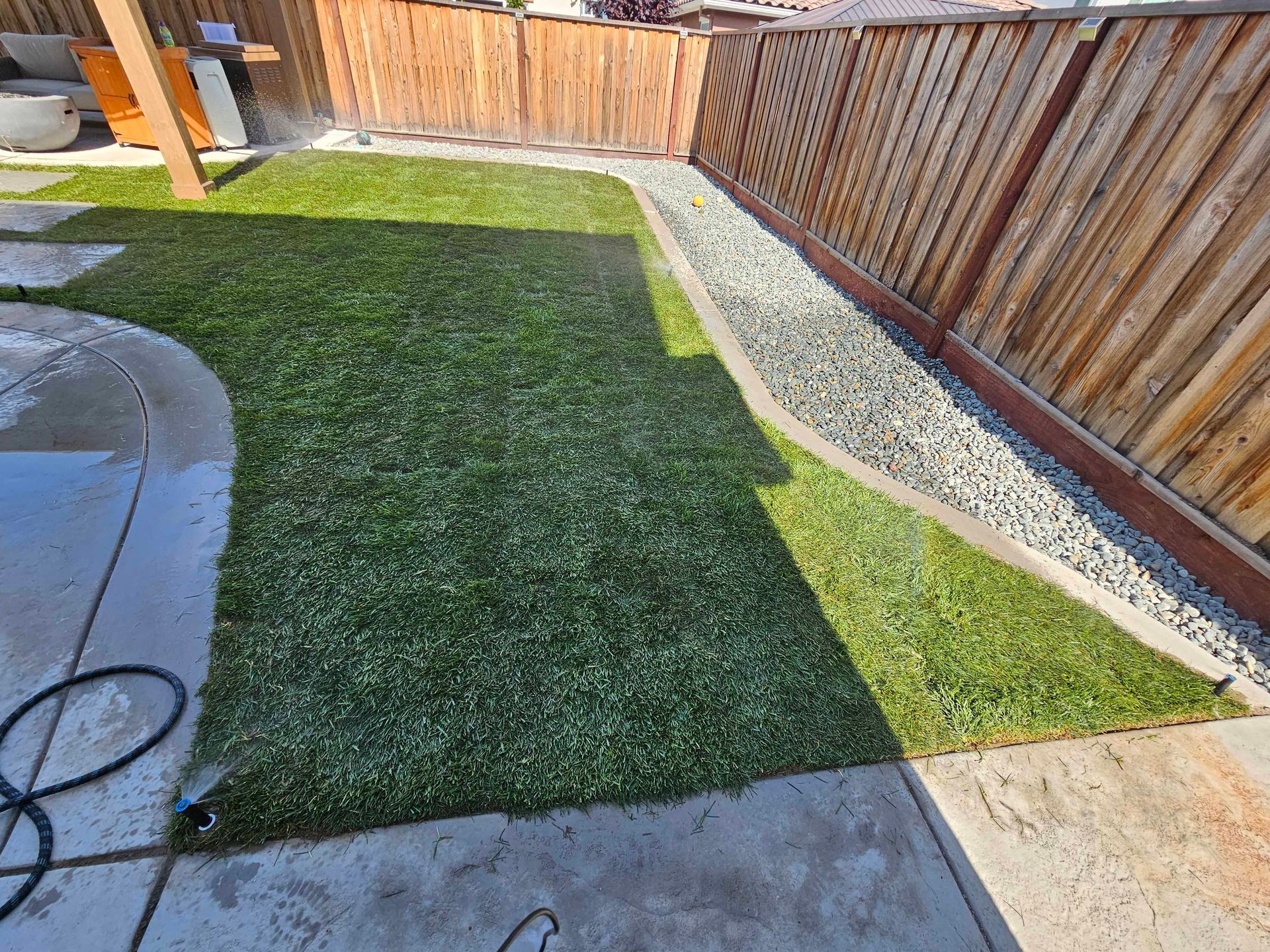 Green lawn and gravel path bordered by a wooden fence and concrete patio.