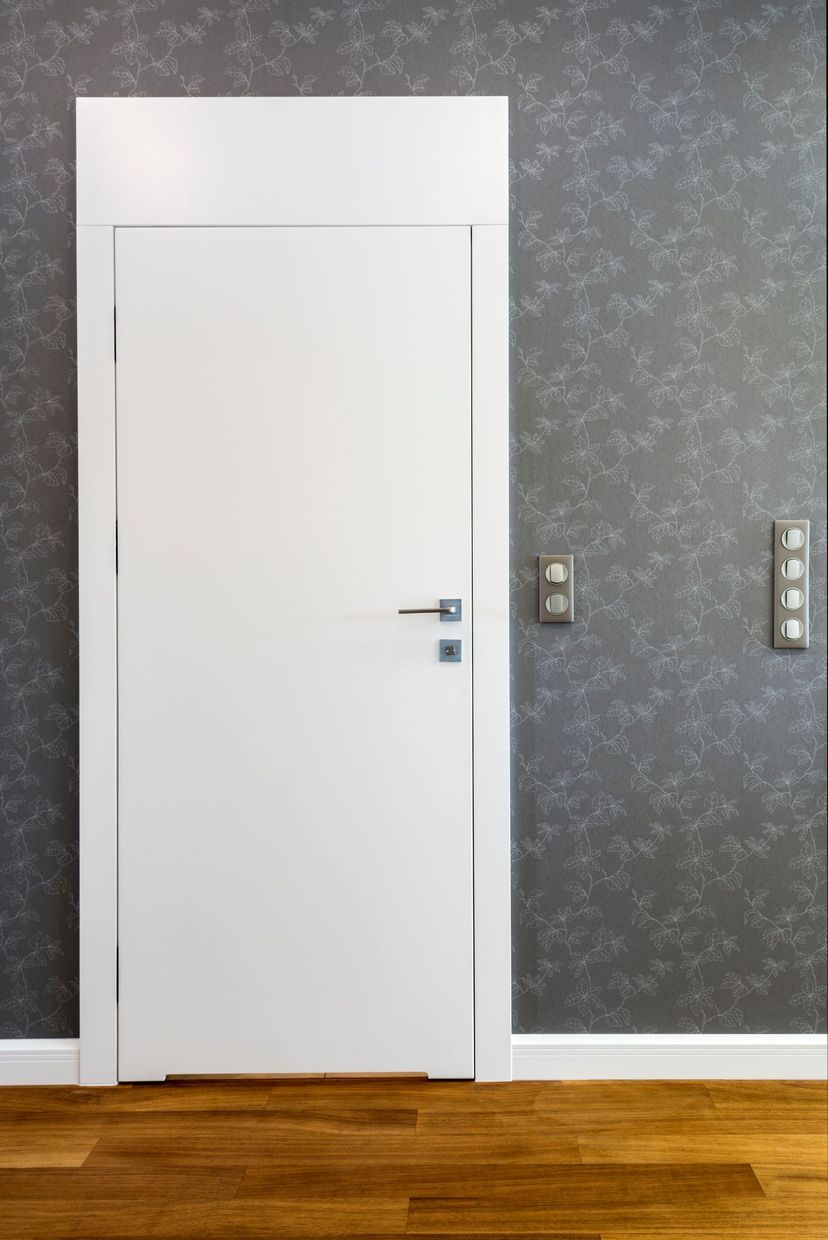 Una porta bianca si trova in una stanza vuota con un pavimento in legno.