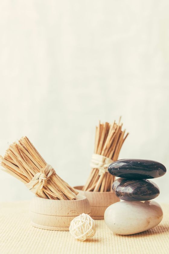 Piedras apiladas, pajitas atadas y una pequeña bola dispuesta para un tratamiento de spa sobre un fondo claro.