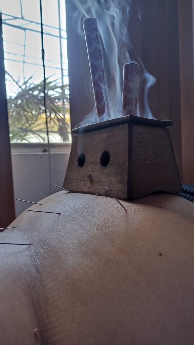 Una caja de moxibustión de madera con varillas humeantes sobre el cuerpo de una persona.