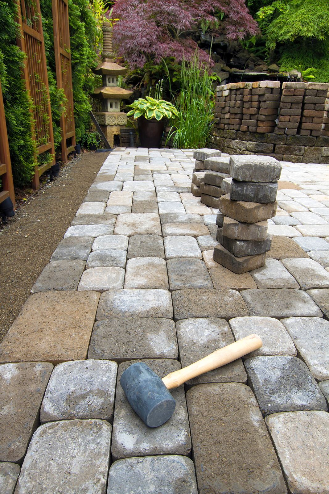 Pathway paving with gray and tan blocks; a mallet and stacks of blocks are visible.