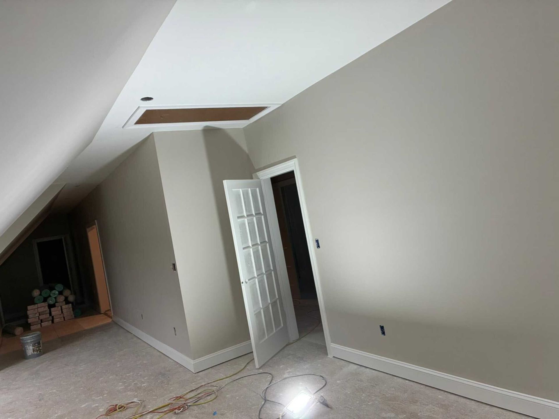Room with white ceiling and tan walls, open door. Construction in progress, bare floor.
