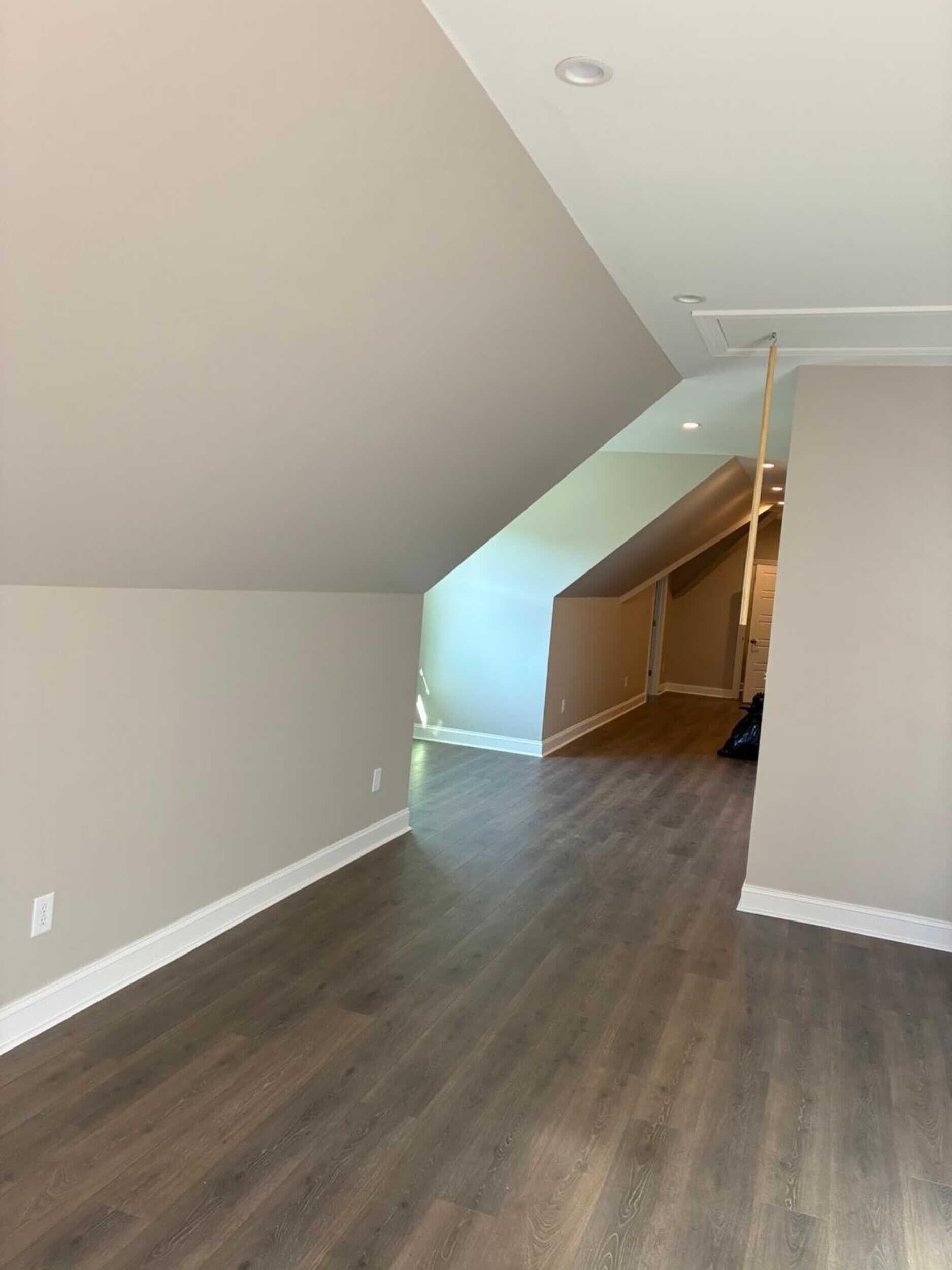 Empty attic room with slanted walls, dark wood-look floor, and a recessed ceiling light.
