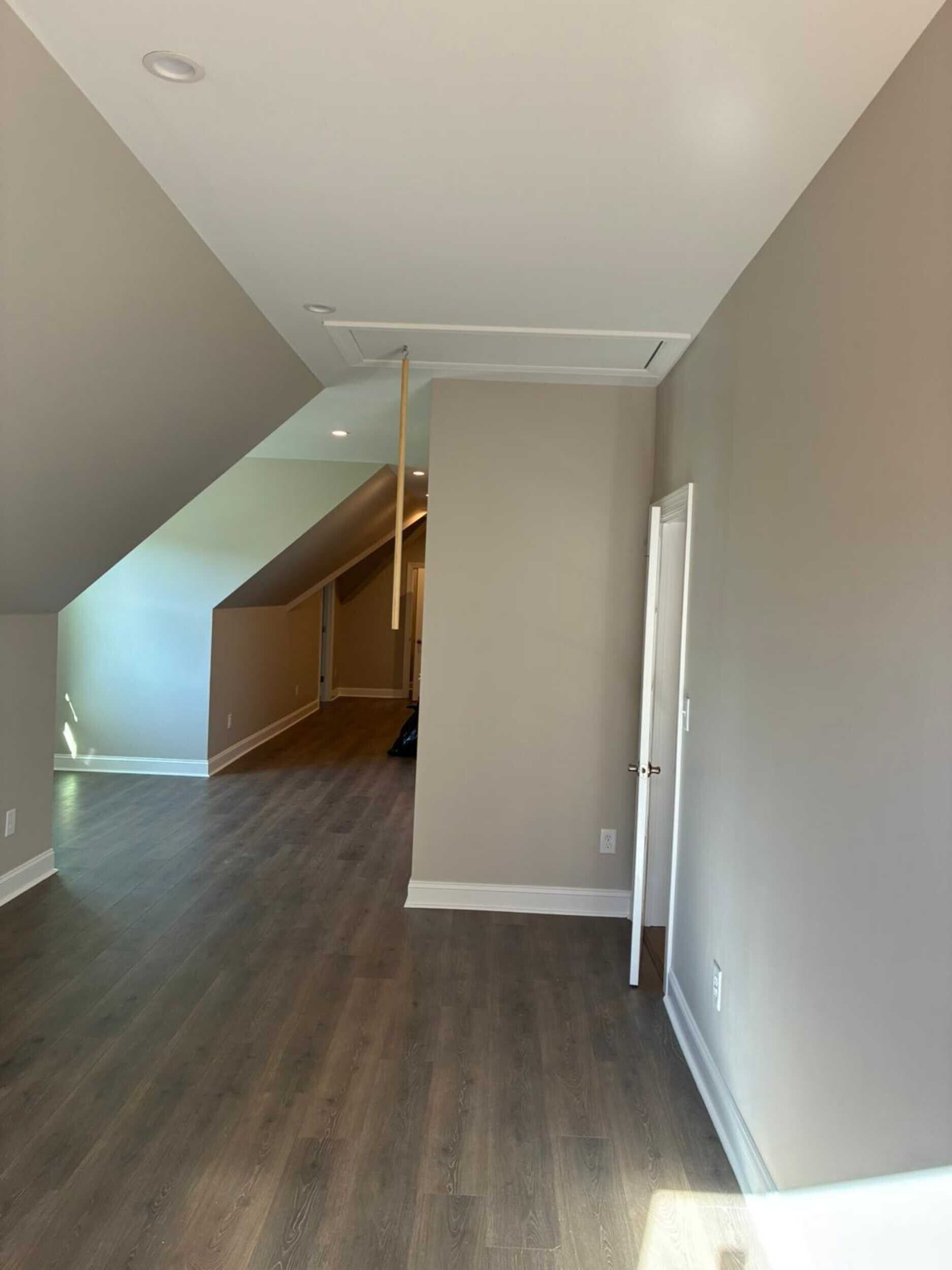 Interior room with sloped ceiling, attic access, and wood flooring. Light gray walls and door frame.