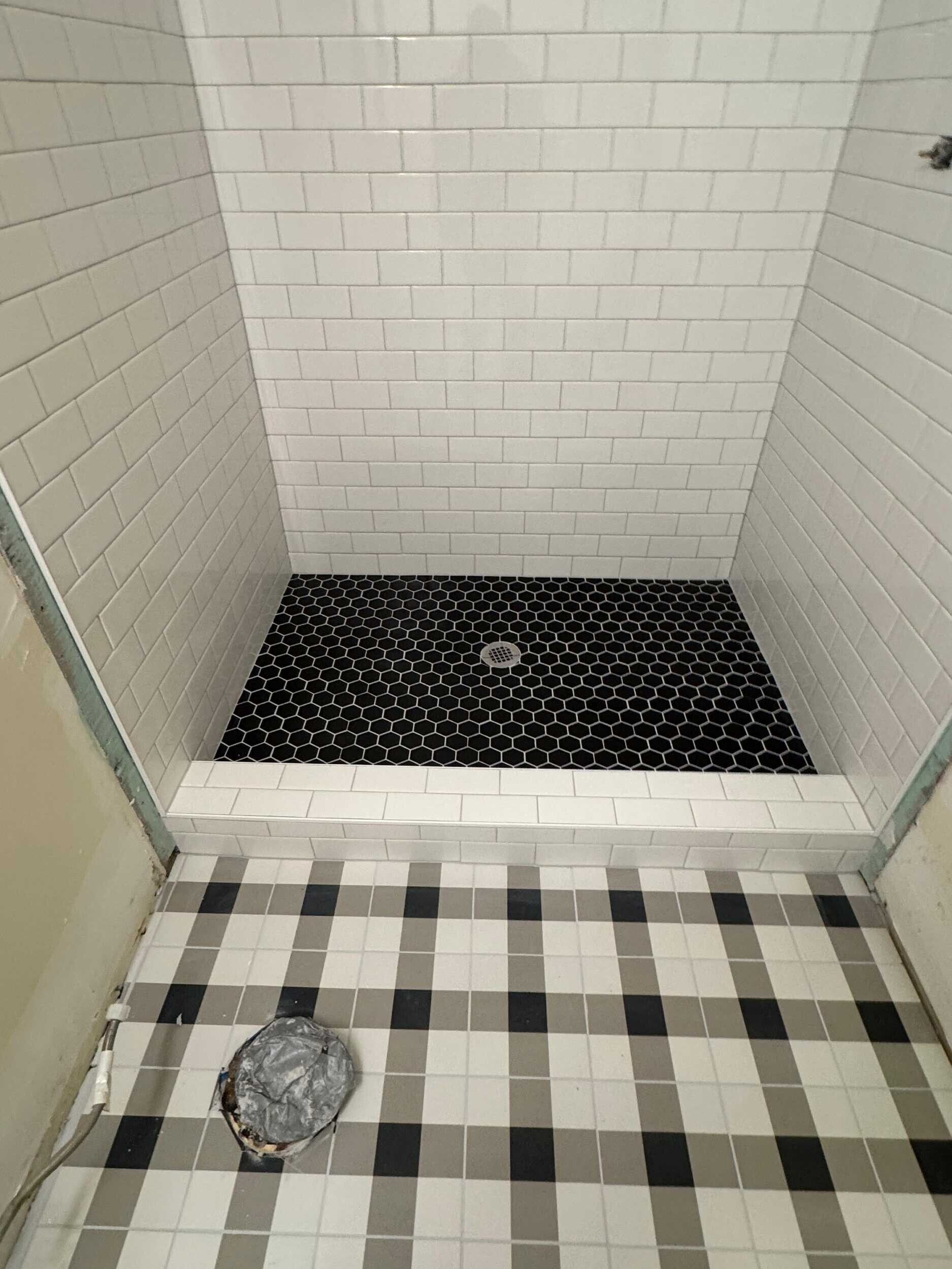 Shower with black and white tile design, including a tiled floor and a pebble-like shower base.