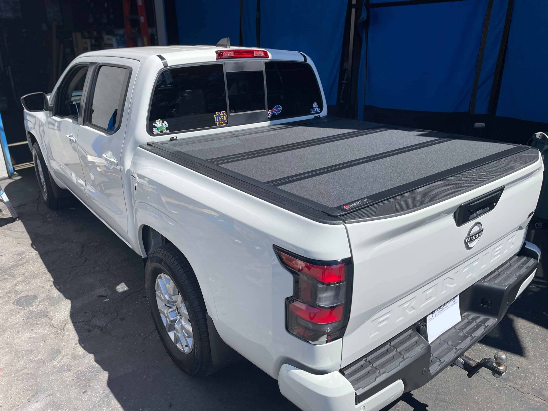 A white truck with a black bed cover is parked in front of a blue building.