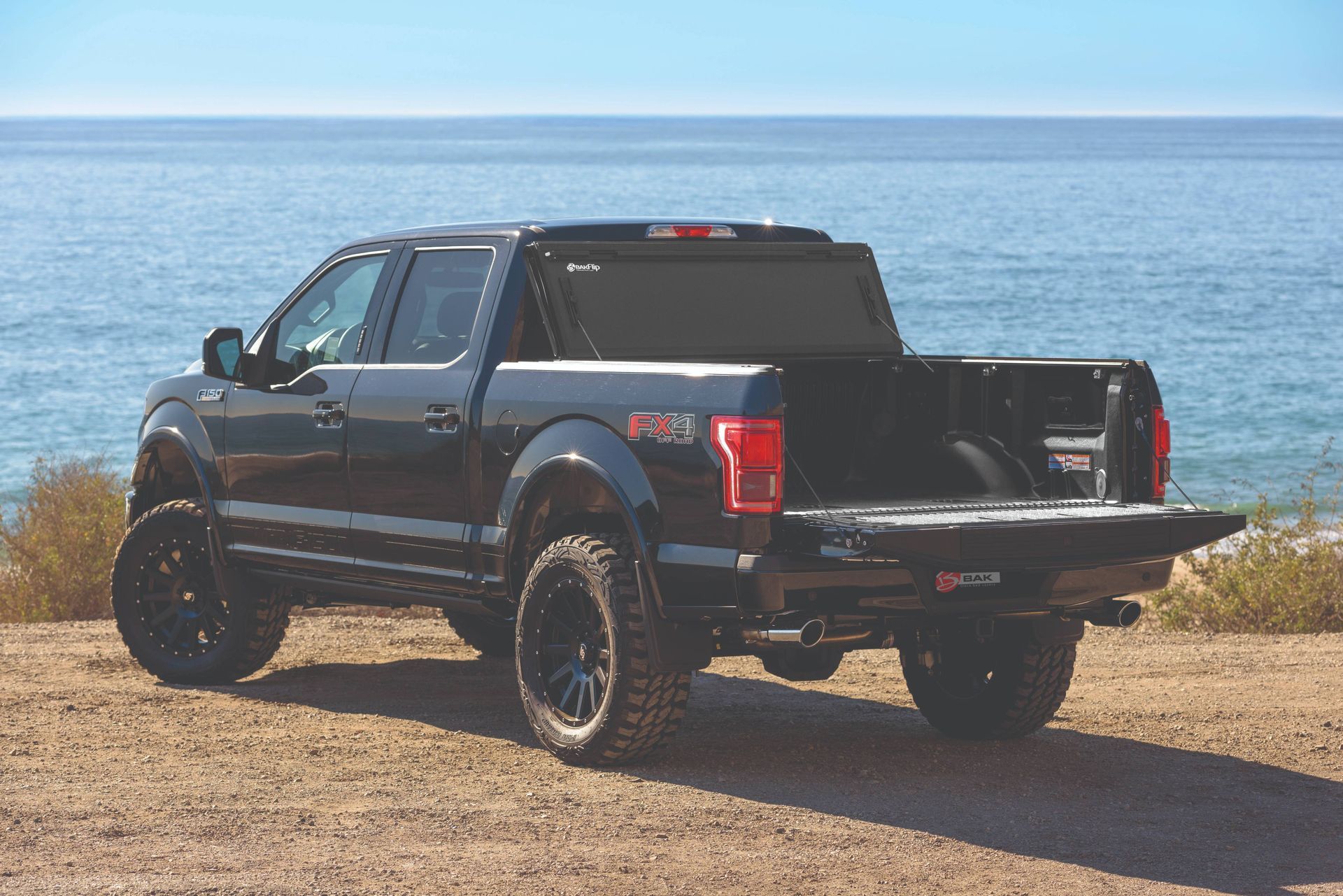 A black pickup truck is parked on a dirt road near the ocean.