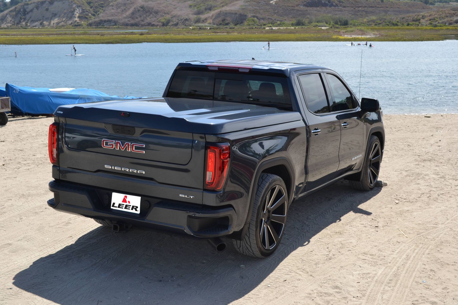 A black gmc truck is parked on a sandy beach next to a body of water.
