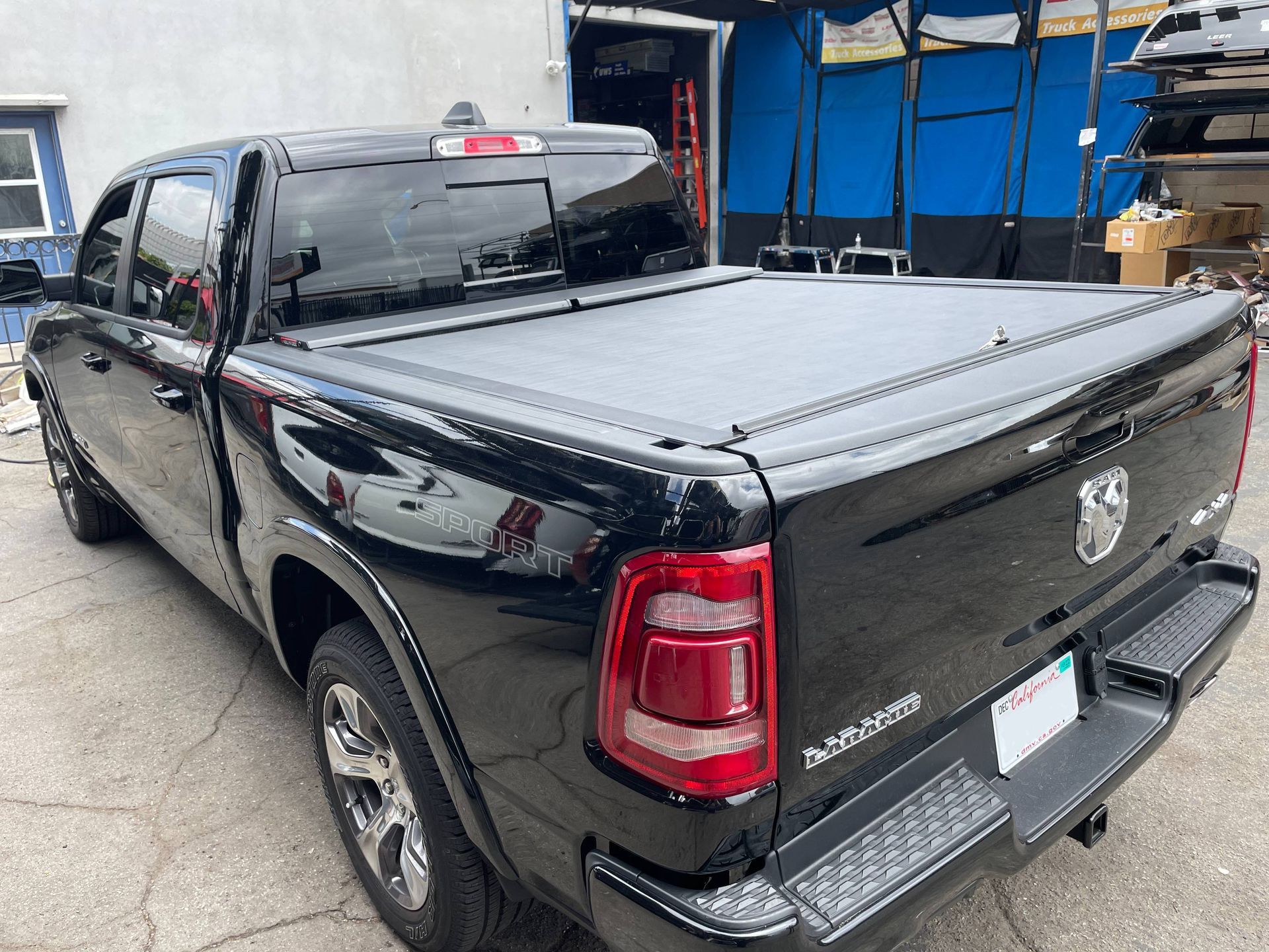 A black dodge ram truck with a black bed cover is parked in front of a building.