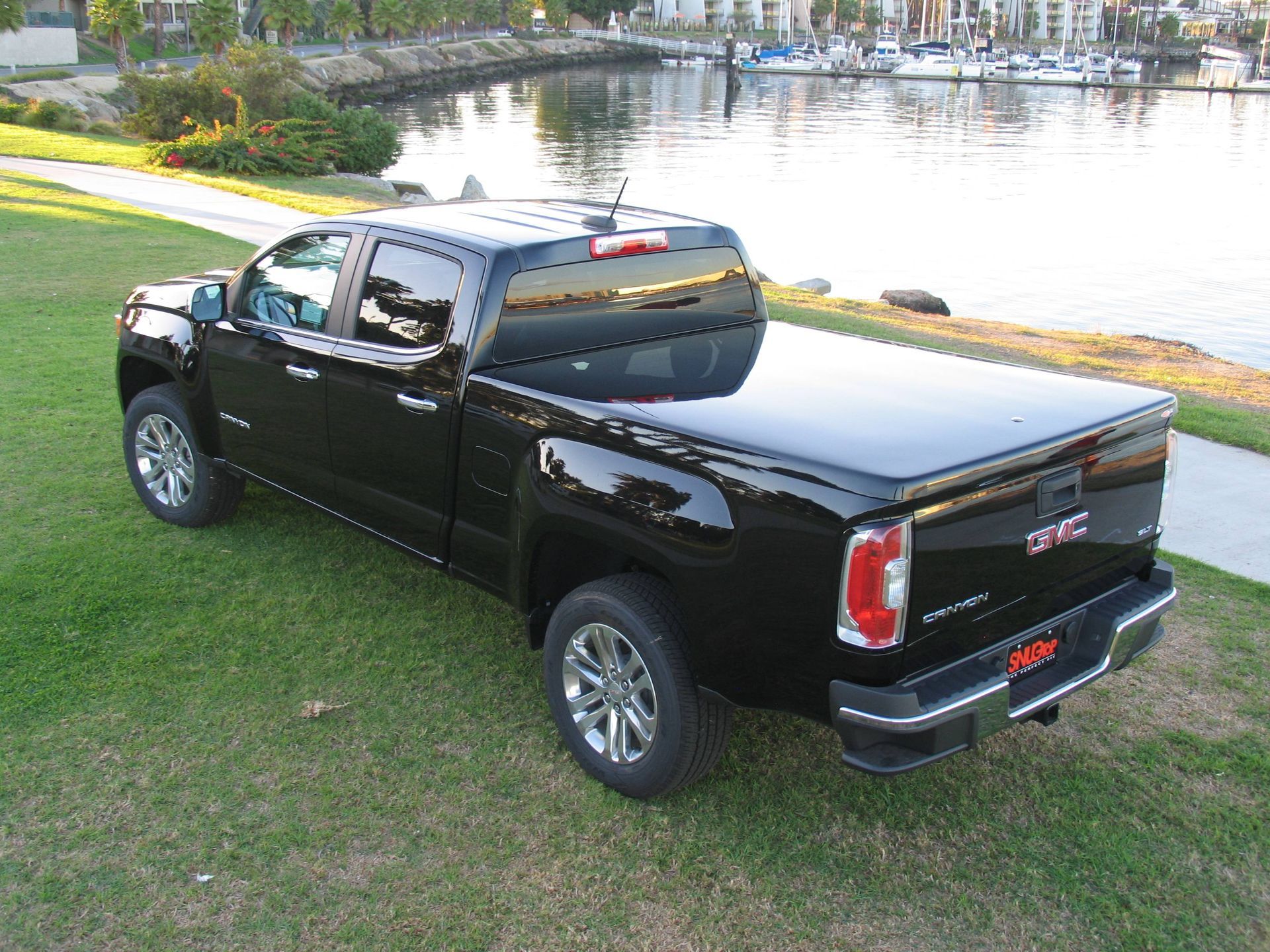 A black gmc truck is parked on the grass near a body of water