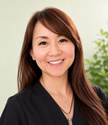 Smiling woman with long brown hair wearing a black top and necklace against a light background