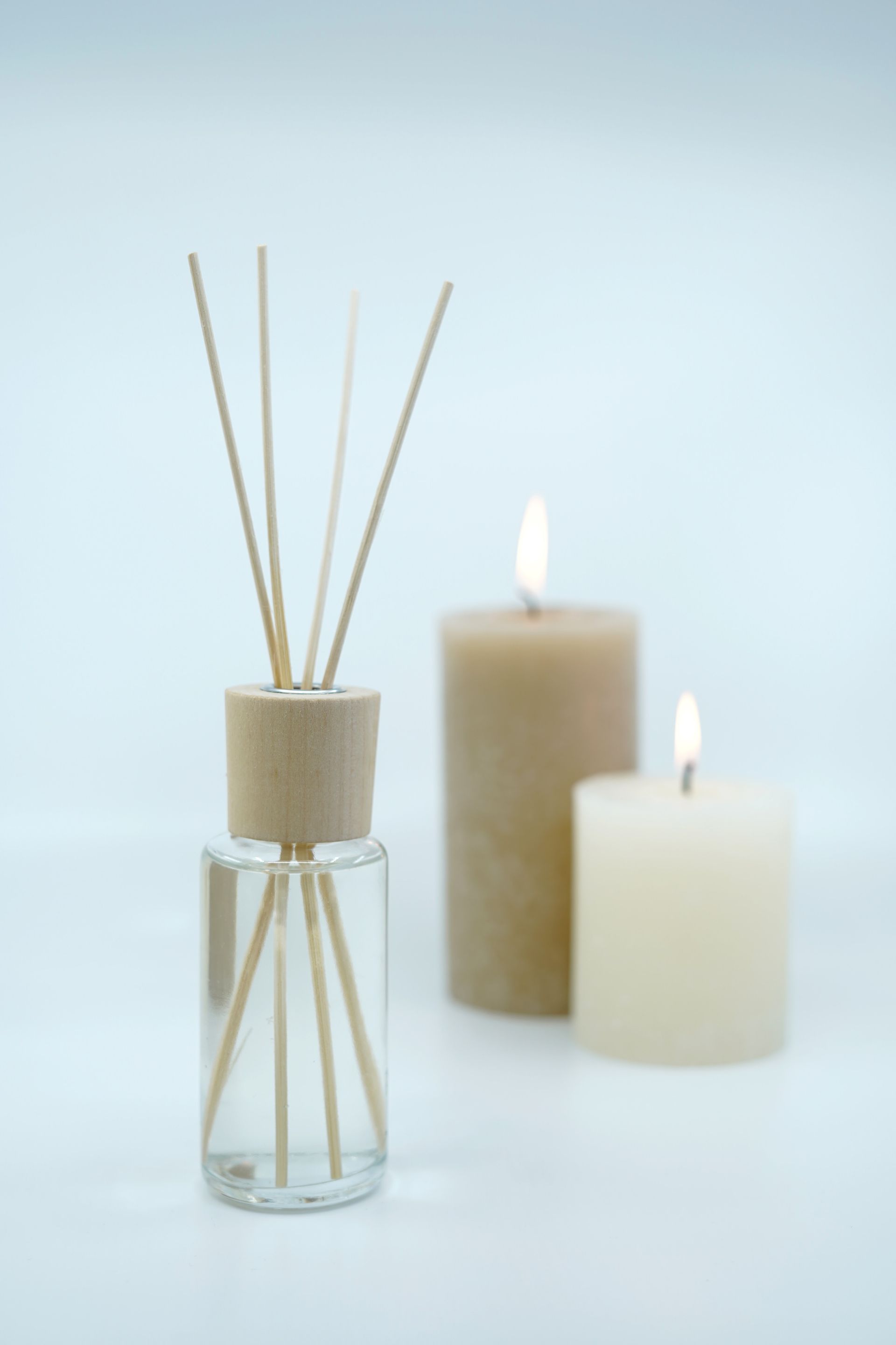 There are two candles in the background and a reed diffuser in the foreground.