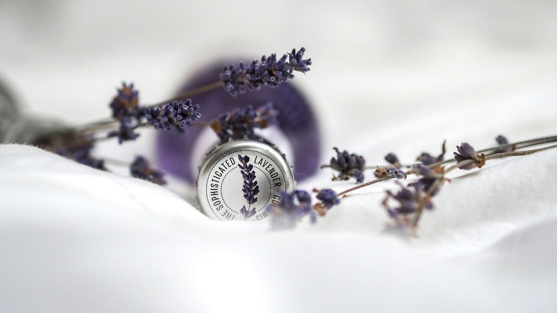 a bottle of lavender essential oil is sitting on a white towel next to a bunch of lavender flowers .