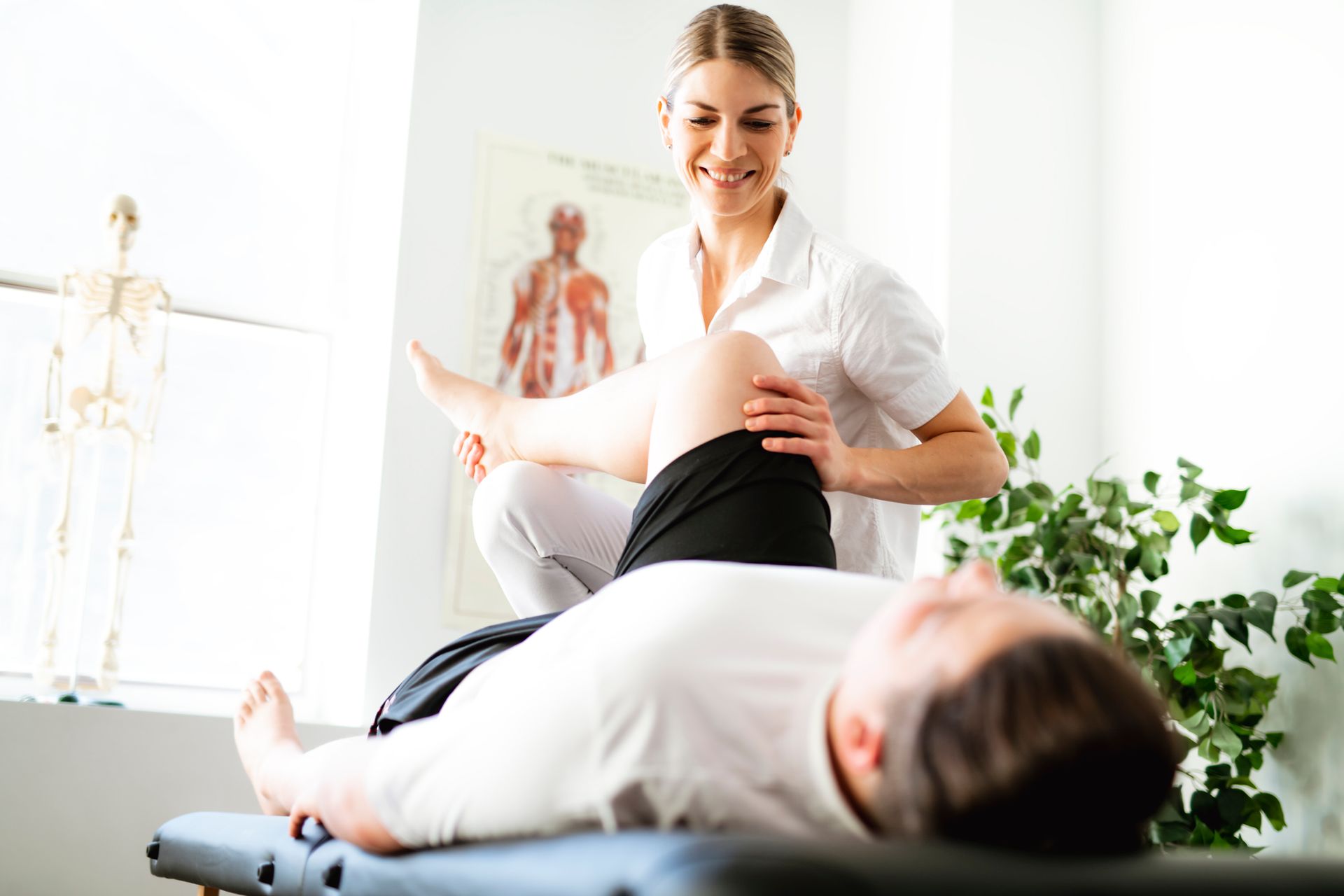 A woman is stretching a man 's leg on a table.