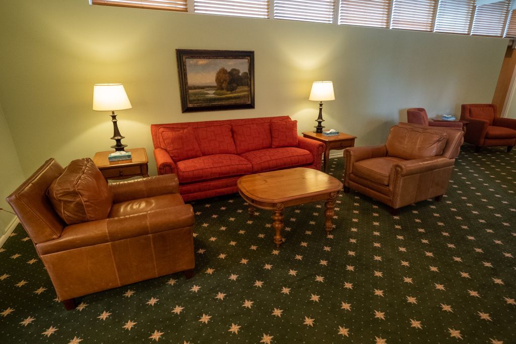 a living room with a red couch , two chairs , a coffee table and a painting on the wall .