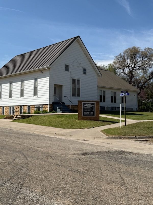 A white house with a brown roof is on the corner of a street.
