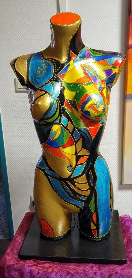 Auf einem Tisch sitzt eine farbenfrohe Statue eines Frauentorsos.