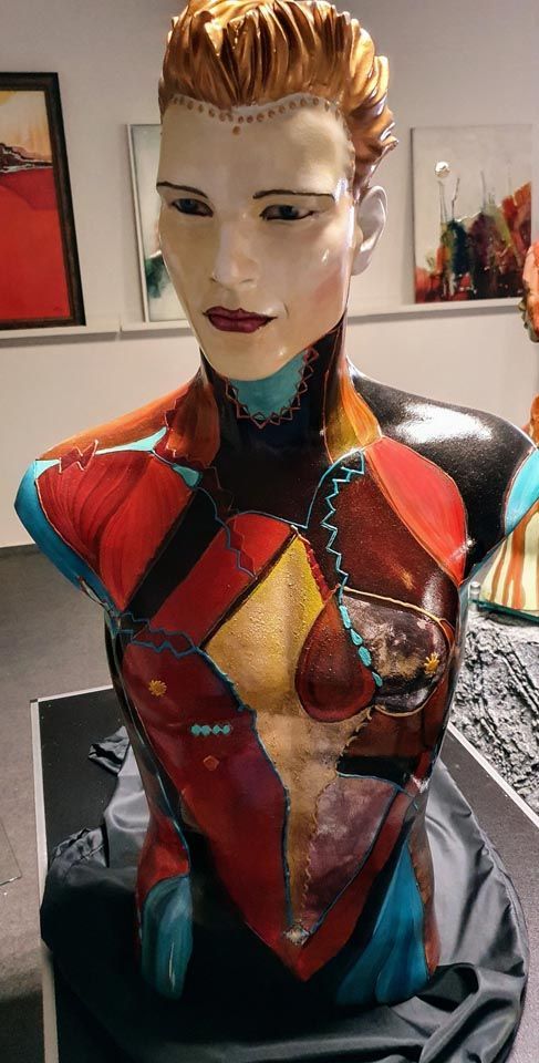 Auf einem Tisch sitzt eine farbenfrohe Statue eines Frauentorsos.