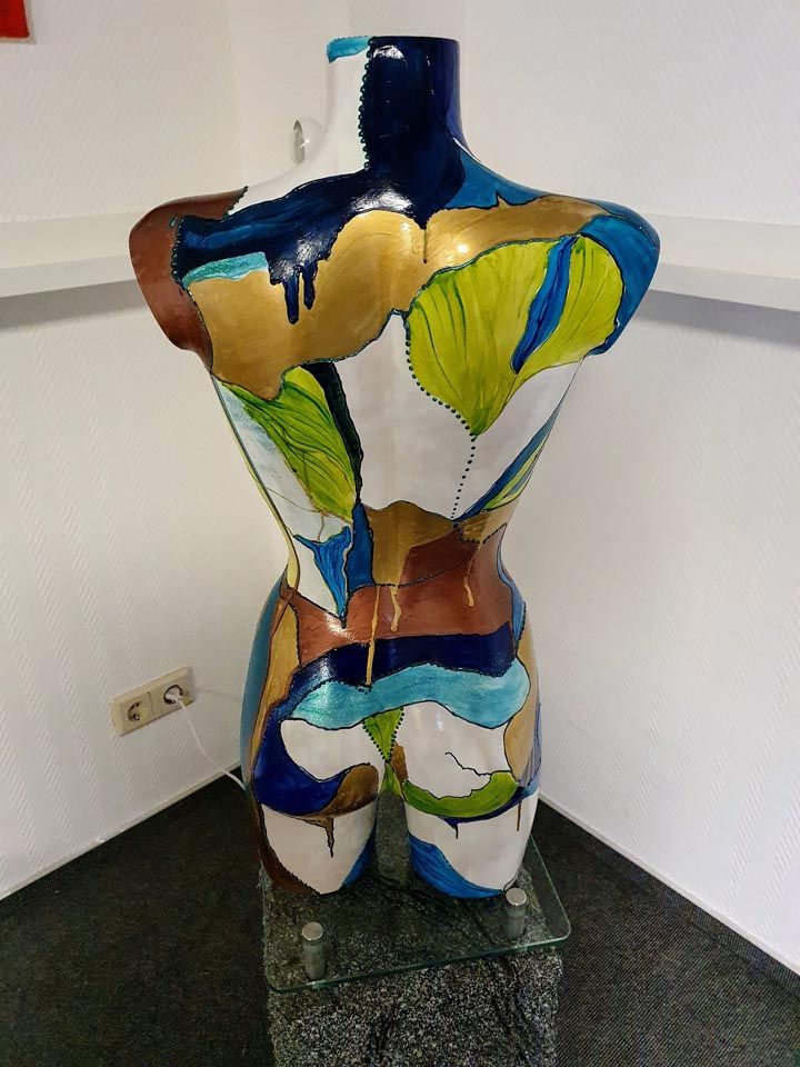 Eine bunte Statue eines Frauentorsos sitzt auf einem Glastisch