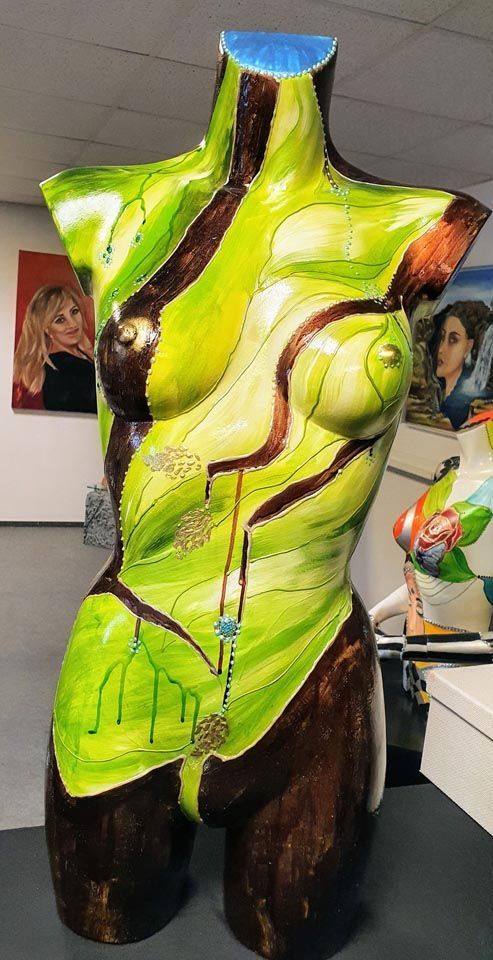 Auf einem Tisch sitzt eine grün-braune Statue eines Frauentorsos.