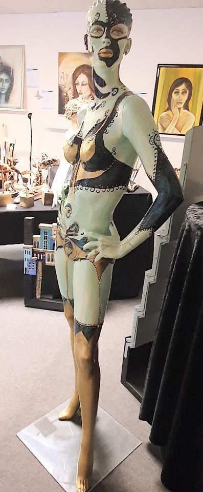 In einem Raum steht die Statue einer Frau mit einer Maske im Gesicht.