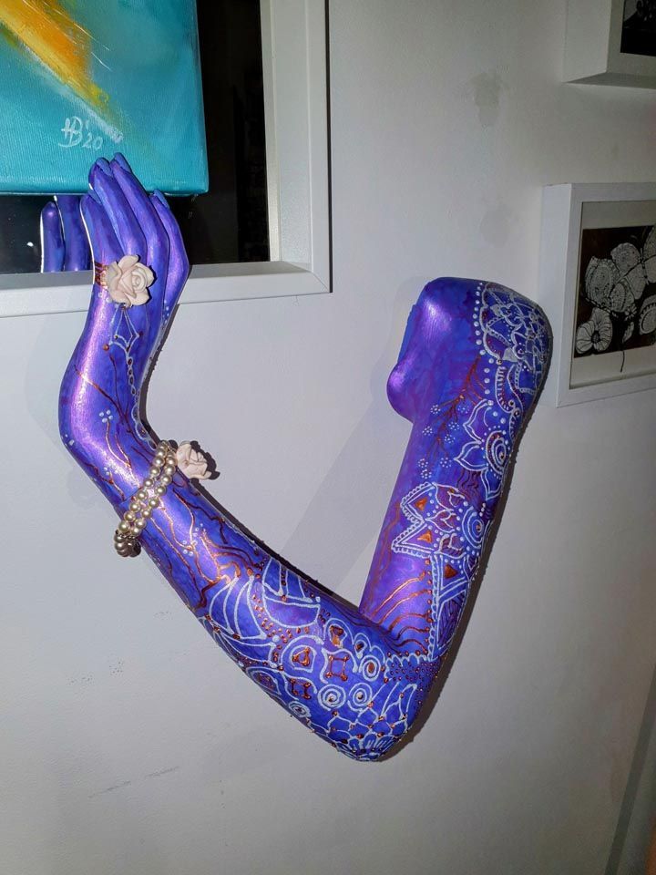 An einer Wand hängt eine violette Statue eines Frauenarms.