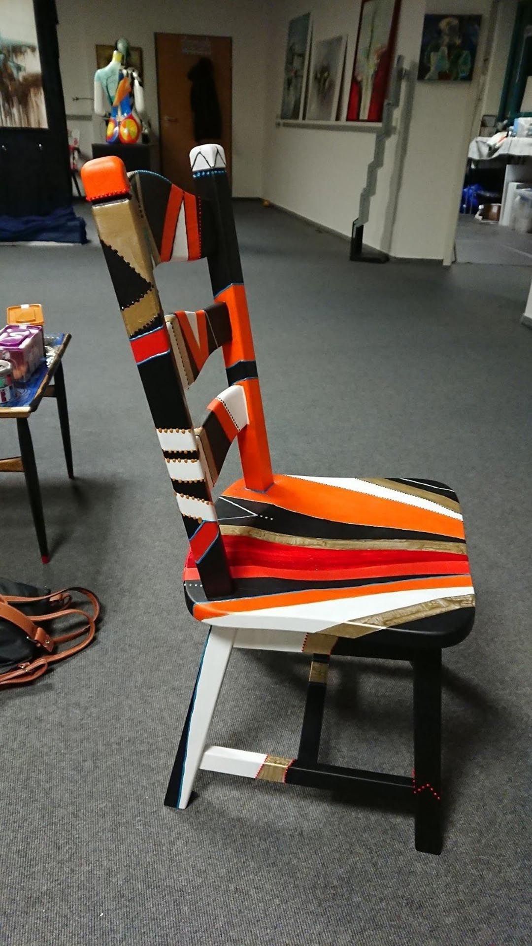 In einem Zimmer steht ein bunter Stuhl auf einem mit Teppichboden ausgelegten Boden.