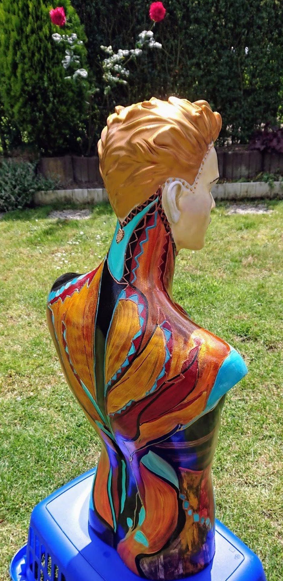 Eine farbenfrohe Statue eines Männertorsos sitzt auf einem blauen Hocker.