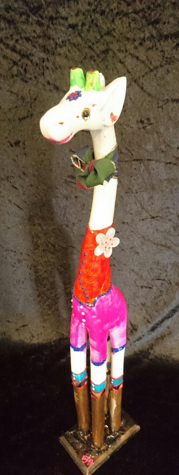 Eine Statue einer Giraffe mit rosa Hosen und grünem Hut.