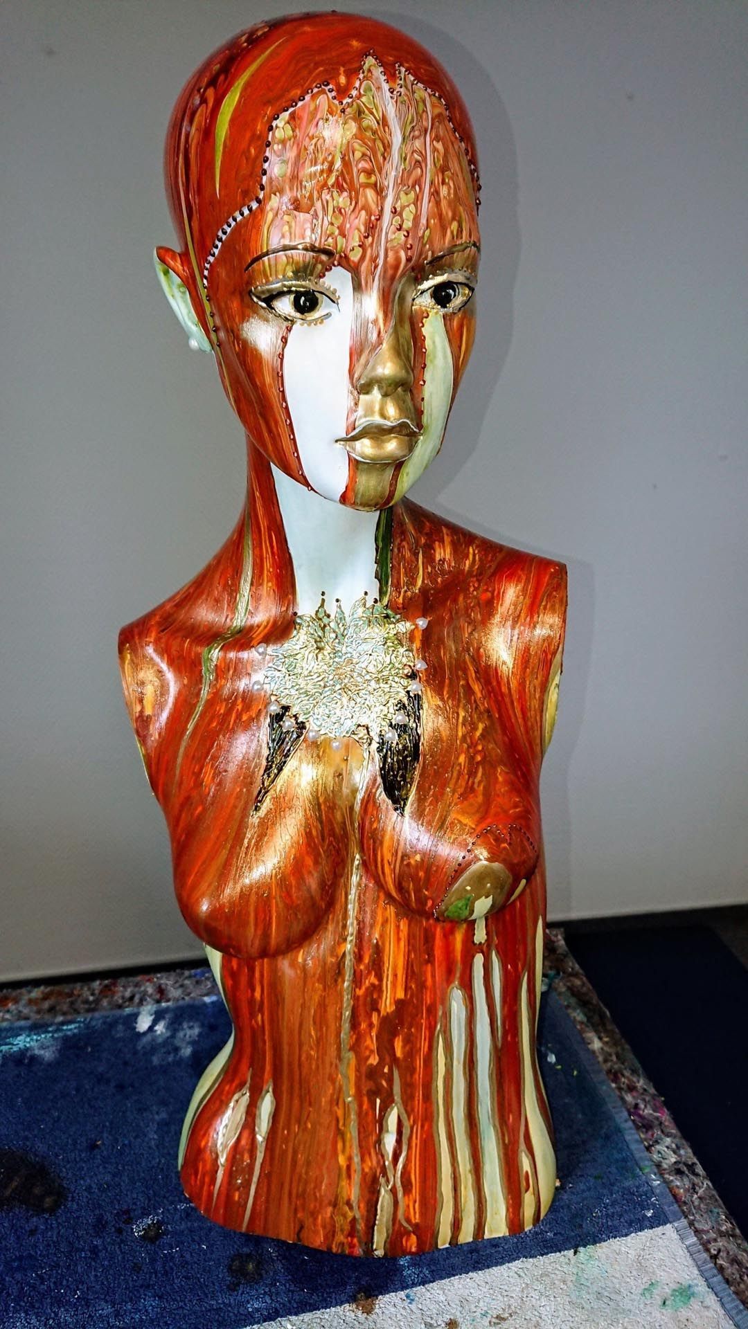 Auf einem Tisch sitzt die Statue einer Frau mit roter und weißer Gesichtsbemalung.