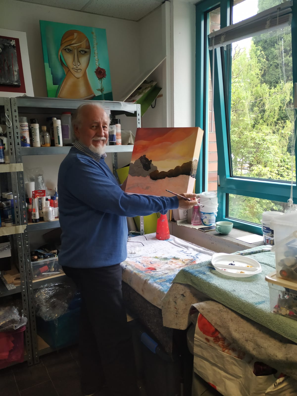 Ein Mann steht vor einem Tisch und hält ein Gemälde in der Hand.