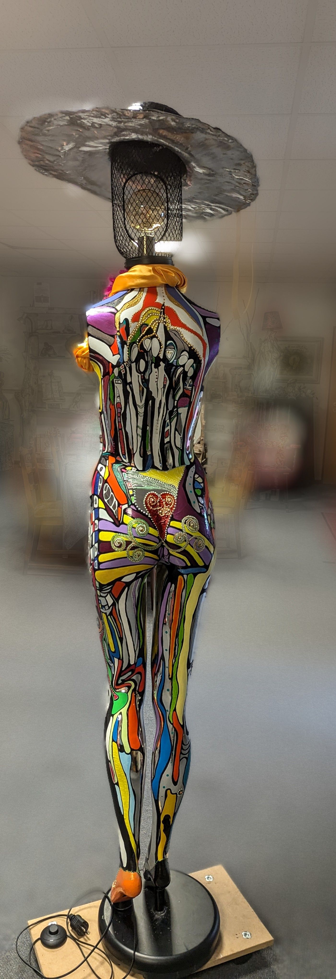 Auf einem Tisch sitzt eine farbenfrohe Statue einer Frau mit Hut.