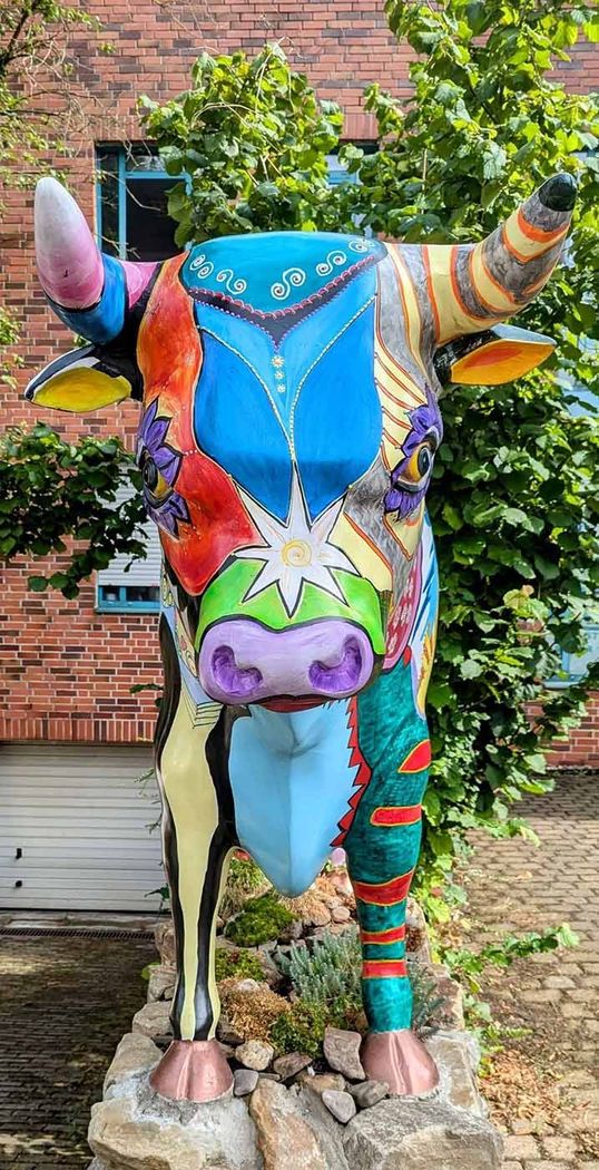 Eine farbenfrohe Stierstatue steht vor einem Backsteingebäude.