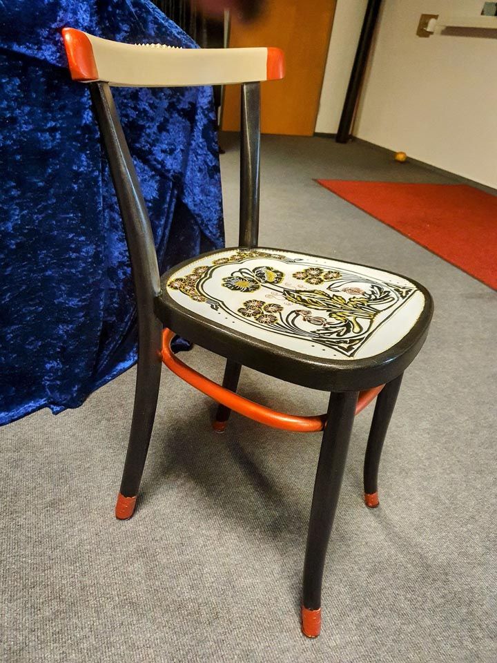 Ein Stuhl mit einem Blumenmuster auf der Sitzfläche steht auf einem Teppichboden.