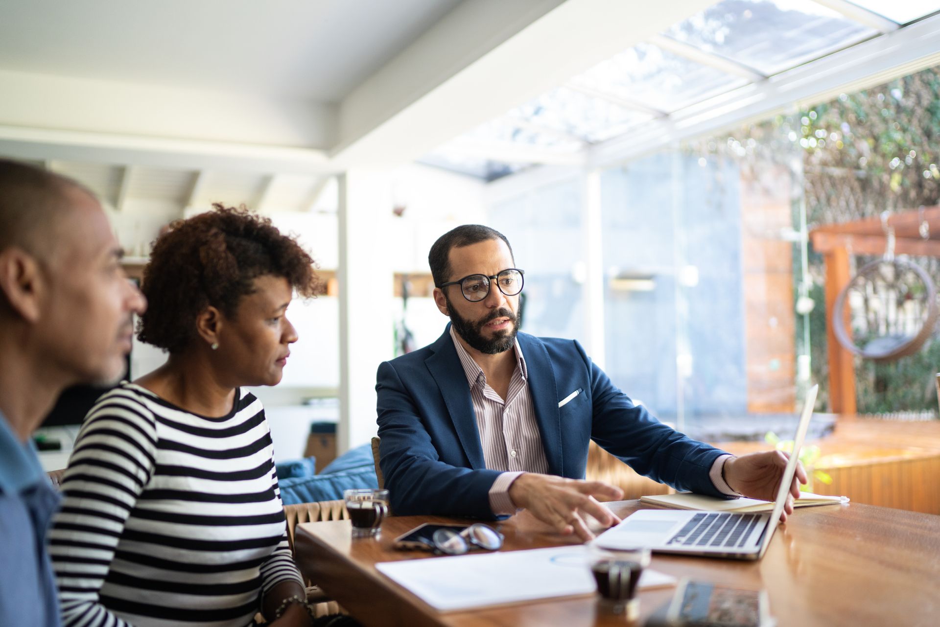 A man and a woman are sitting at a table looking at a laptop.