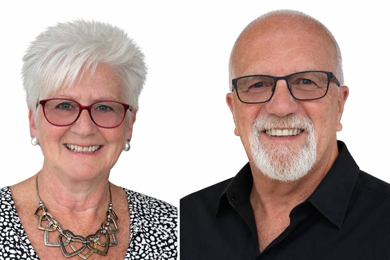Couple, a man with a white beard and a woman with red hair, smiling outside a building.