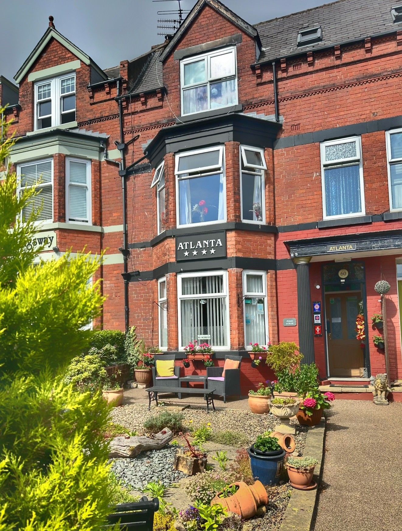 Red brick building with bay windows, small front garden with plants and seating. 