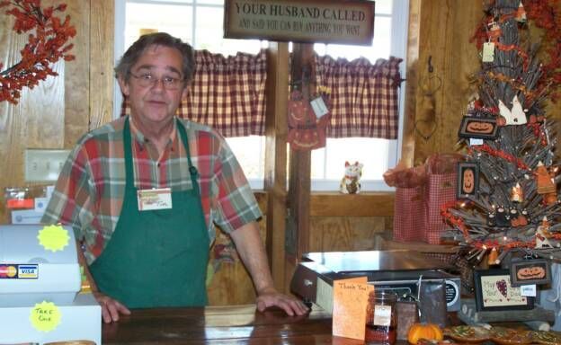 A man in an apron stands behind a counter in front of a christmas tree