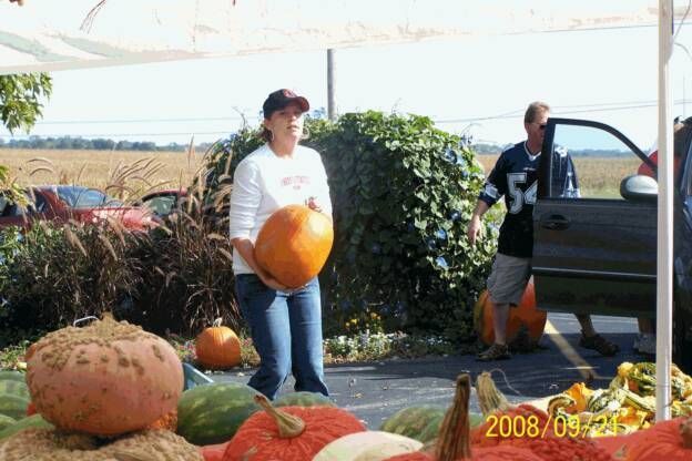 A woman is holding a large pumpkin in a parking lot