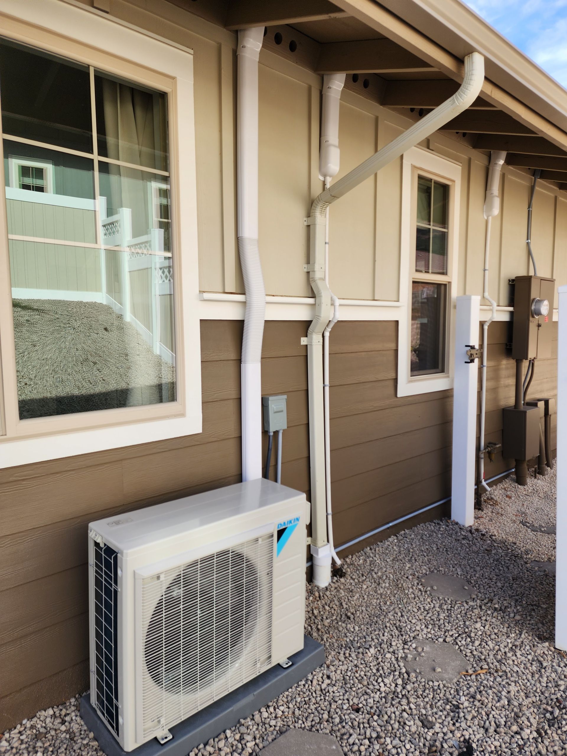 An air conditioner is sitting outside of a house next to a window.