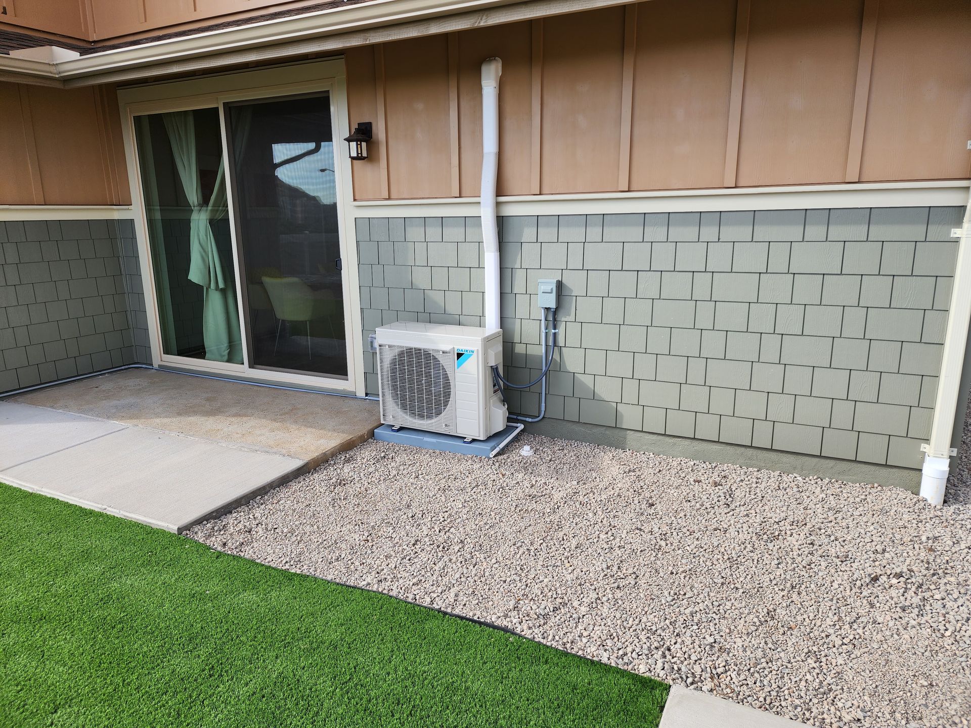 A small air conditioner is sitting on the side of a house next to a sliding glass door.