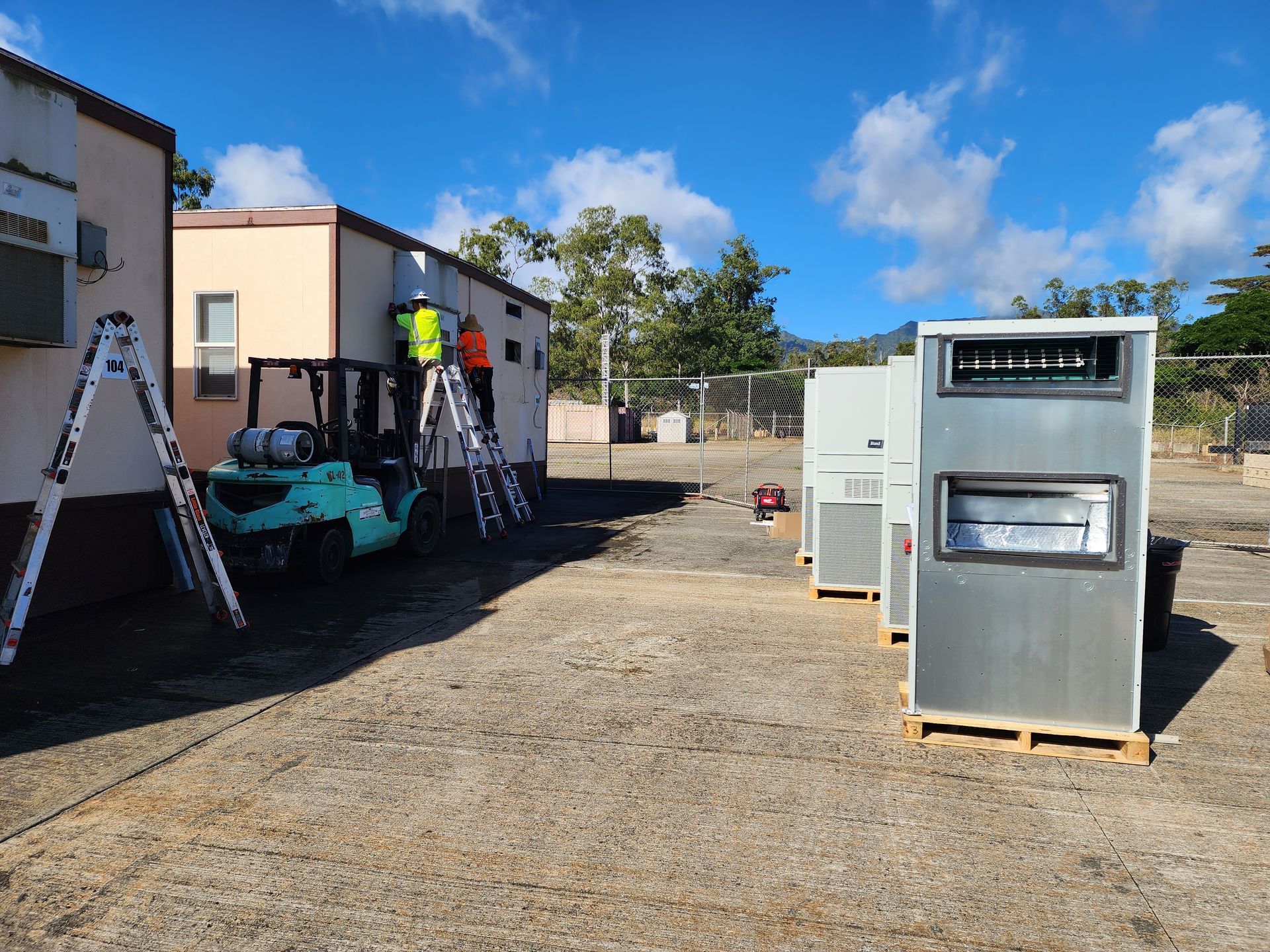 A forklift is parked in front of a building with a ladder in the background.