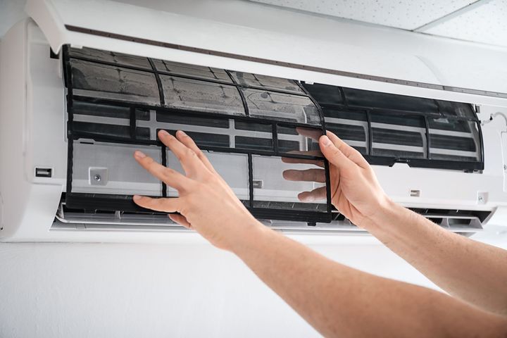 Hands removing a dirty air conditioner filter during maintenance and cleaning process.
